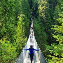 Girl crossing suspension bridge surrounded by tall green trees in Vancouver, Canada